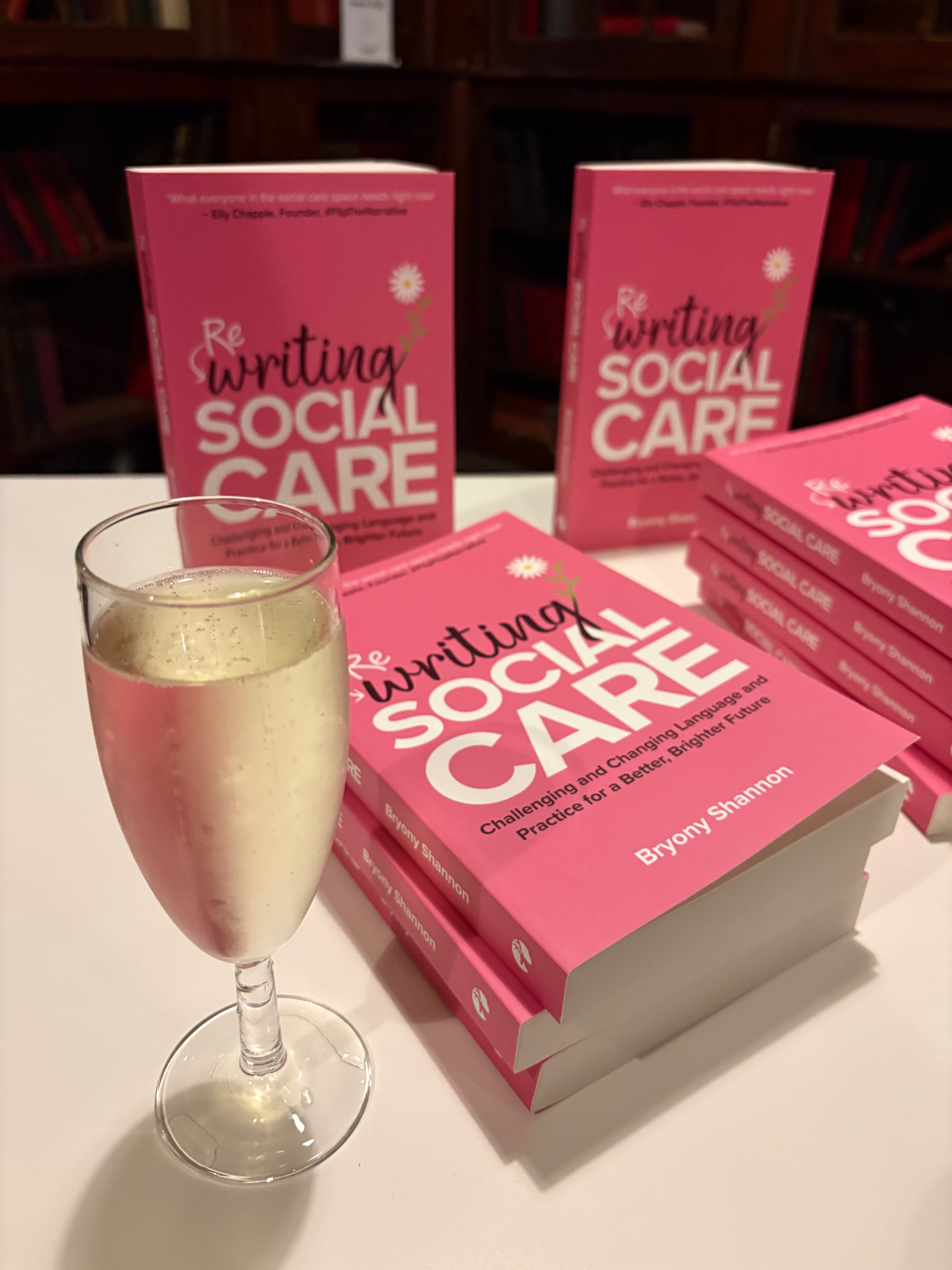 A pile of Rewriting Social Care books next to a glass of Prosecco