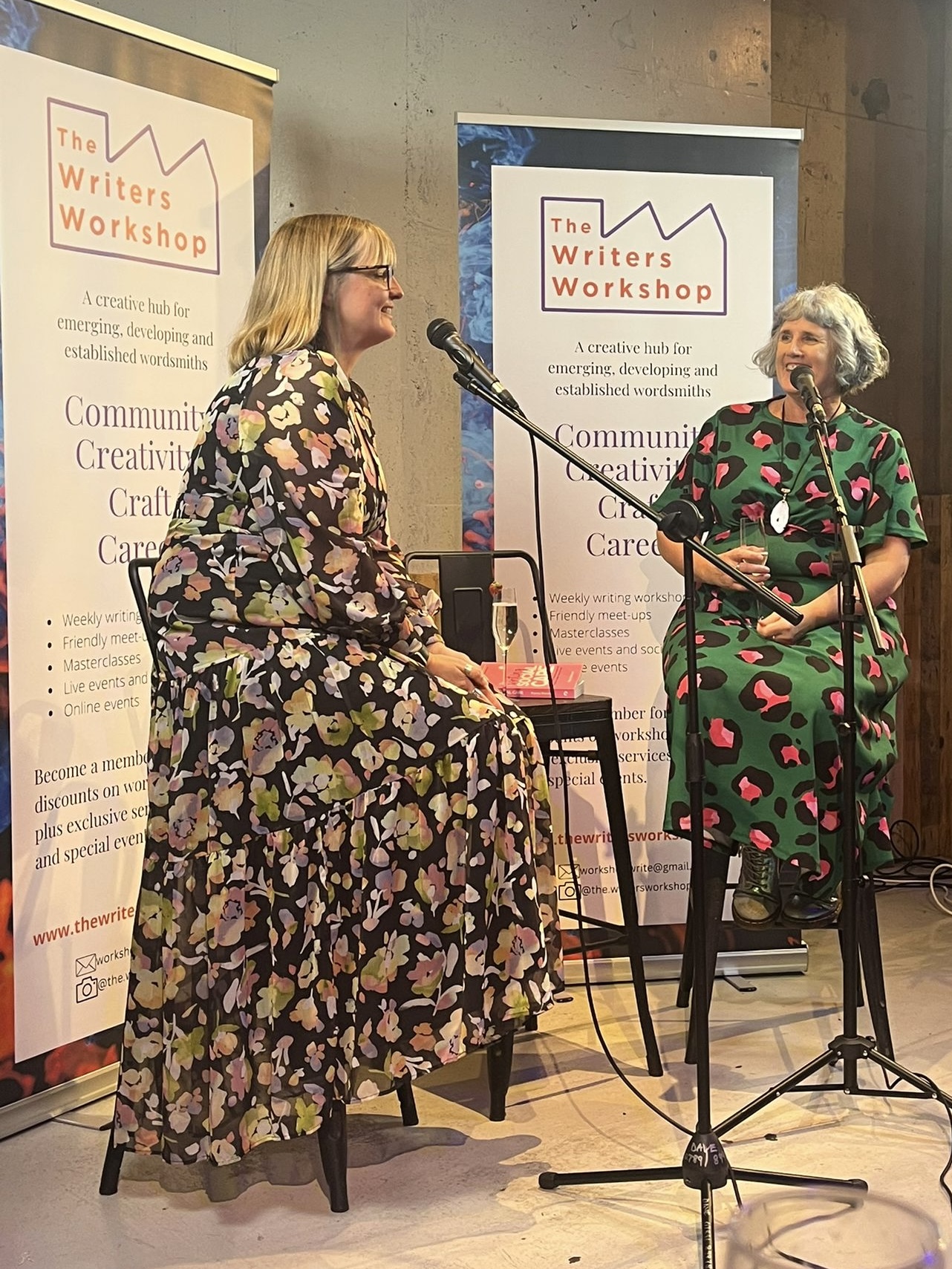 Bryony and Beverley sitting on stools talking in to microphones. They are sitting in front of signs that say 'The Writers Workshop'
